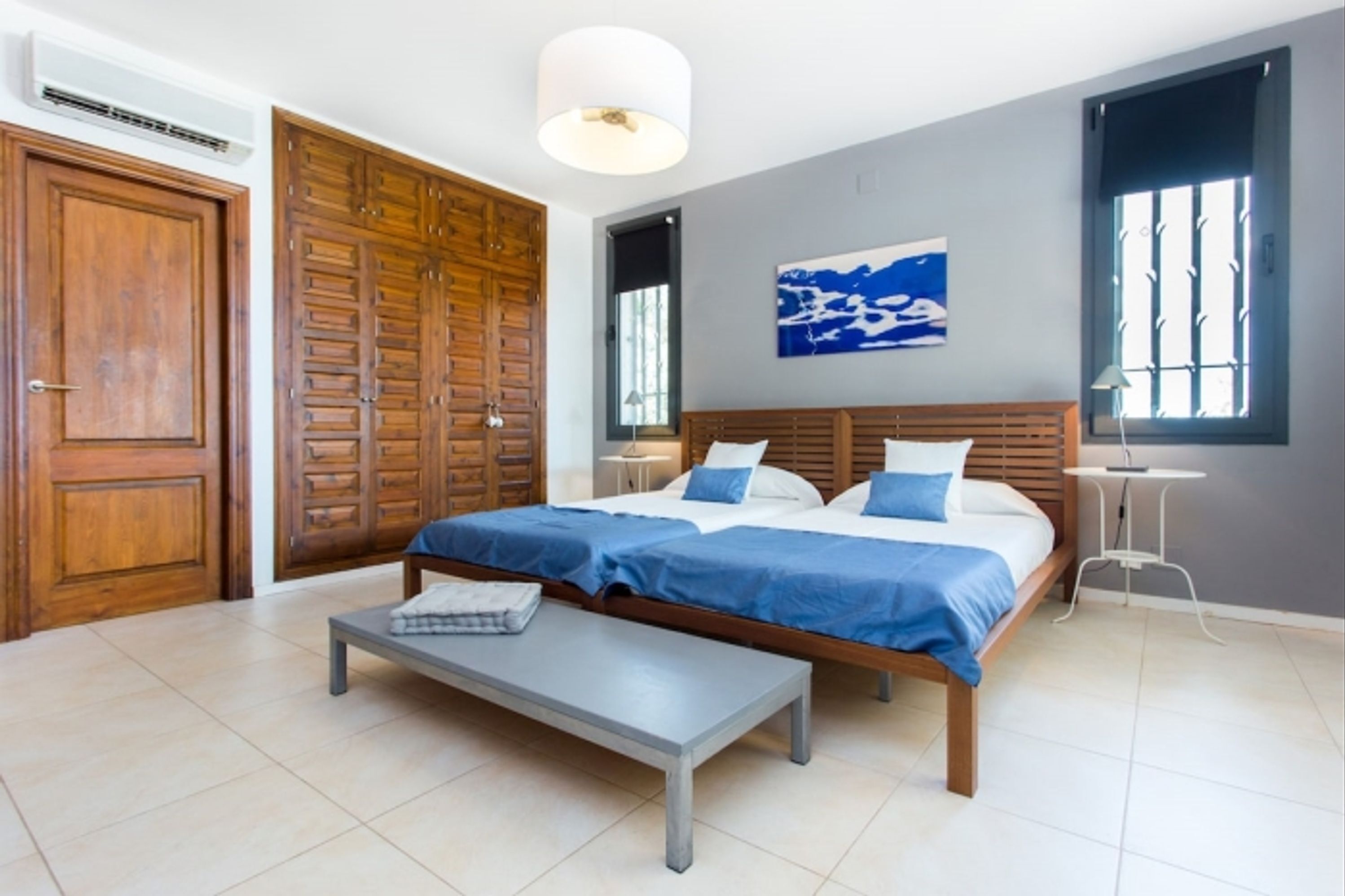 Un dormitorio con cama doble, mesita de noche, banco, armario y ventana con persianas.