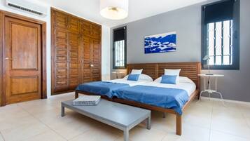 Un dormitorio con cama doble, mesita de noche, banco, armario y ventana con persianas.