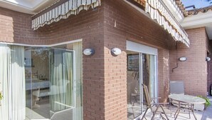 A patio area with a brick wall, sliding glass doors, a white outdoor chair, and a small planter.