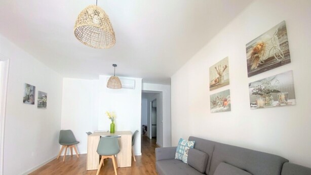 Un salon moderne avec un canapé gris, une table à manger en bois et un luminaire suspendu en fibres tressées.