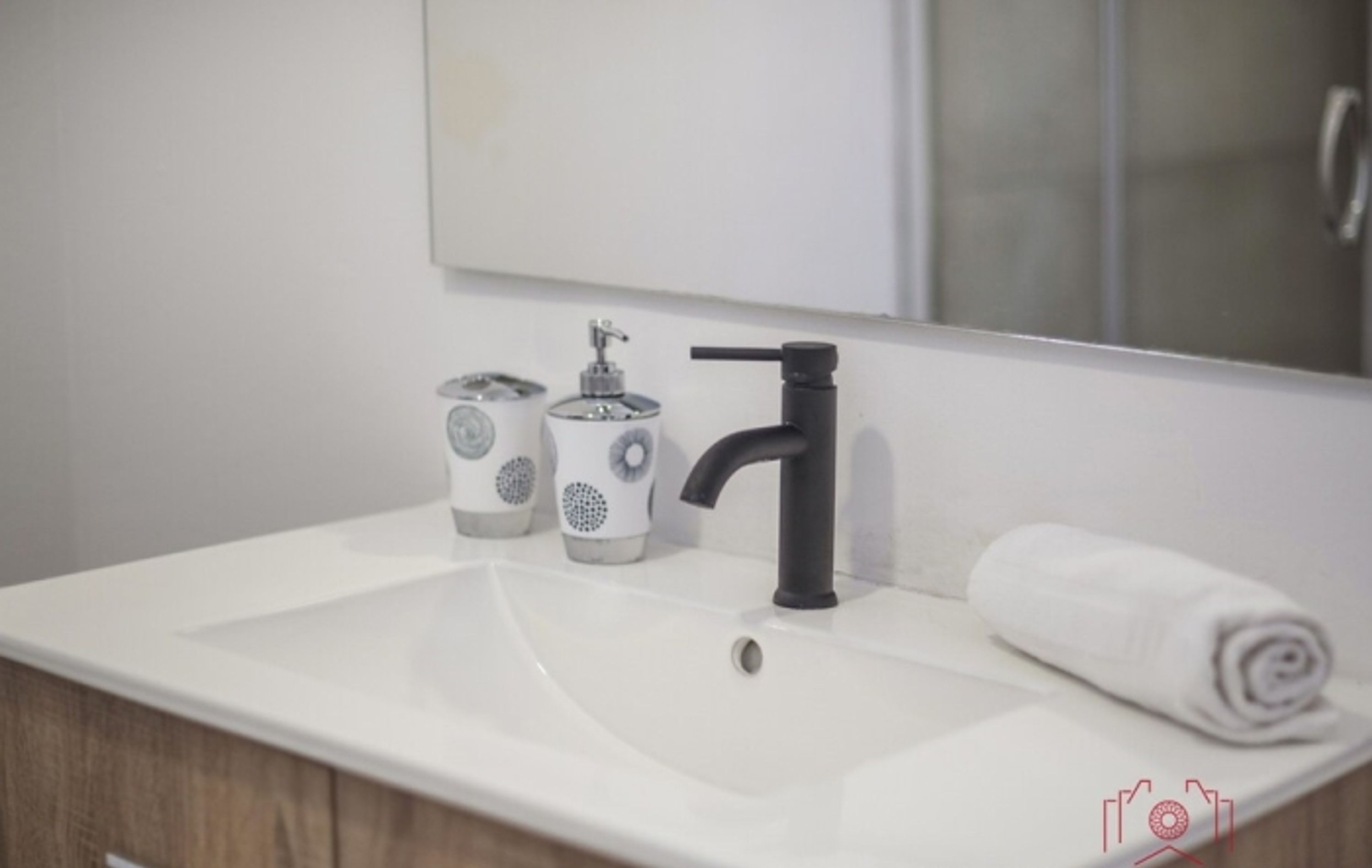 A bathroom with a white sink, black faucet, and two white dispensers with grey patterns.