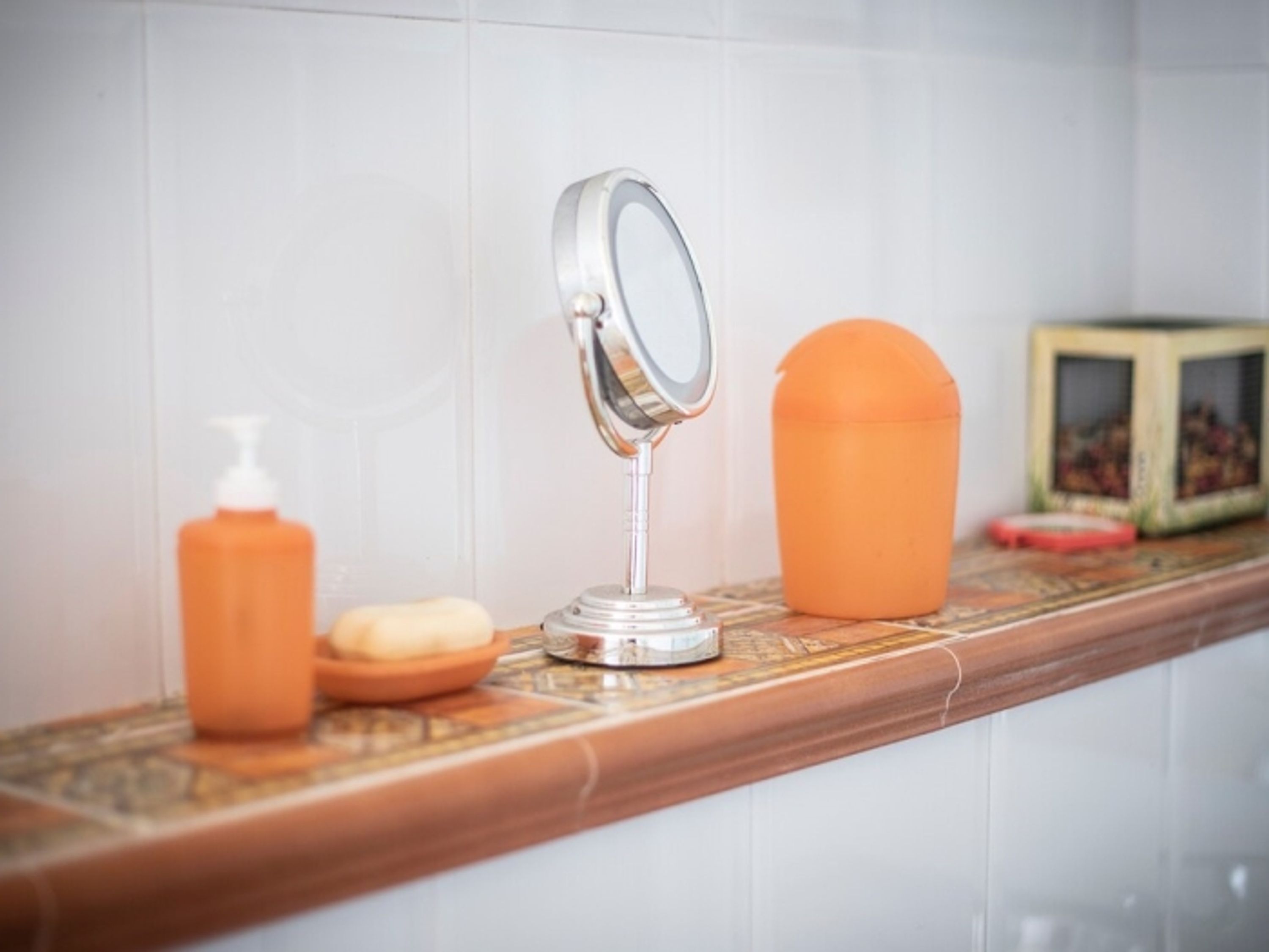 A bathroom vanity with a mirror, soap dispenser, and a small orange container.