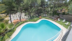 A swimming pool surrounded by trees and a fenced area with lounge chairs.