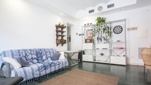 A modern living room with a striped sofa, a coffee table, and a dining area with a white cabinet and shelves. - Th146 Apartamento Elegante Cerca de la Catedral (Tarragona)