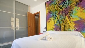A hotel room with a bed, a large colorful tapestry, a wooden door, and a sliding glass door. - Th146 Apartamento Elegante Cerca de la Catedral (Tarragona)