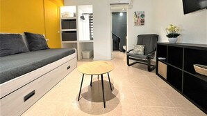 Un salon moderne avec un canapé, une petite table ronde, un fauteuil et un téléviseur fixé au mur.