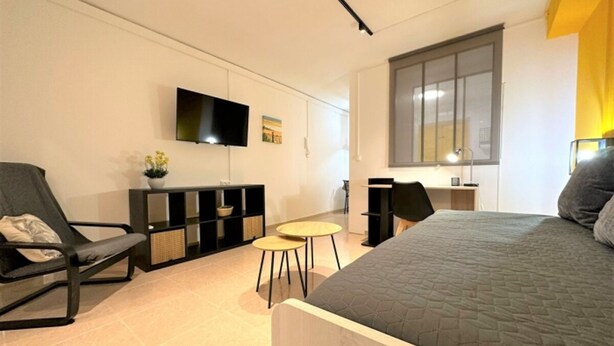 Une chambre moderne avec un grand lit, un bureau, une chaise, une télévision et une fenêtre.