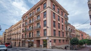 Un edificio de varios pisos con balcones, un paso de peatones y una calle con vehículos.