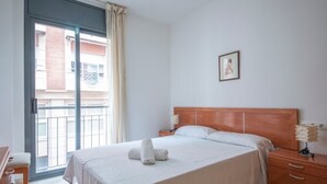 Una habitación de hotel con cama, mesitas de noche, lámpara, un cuadro en la pared y vistas al balcón exterior.