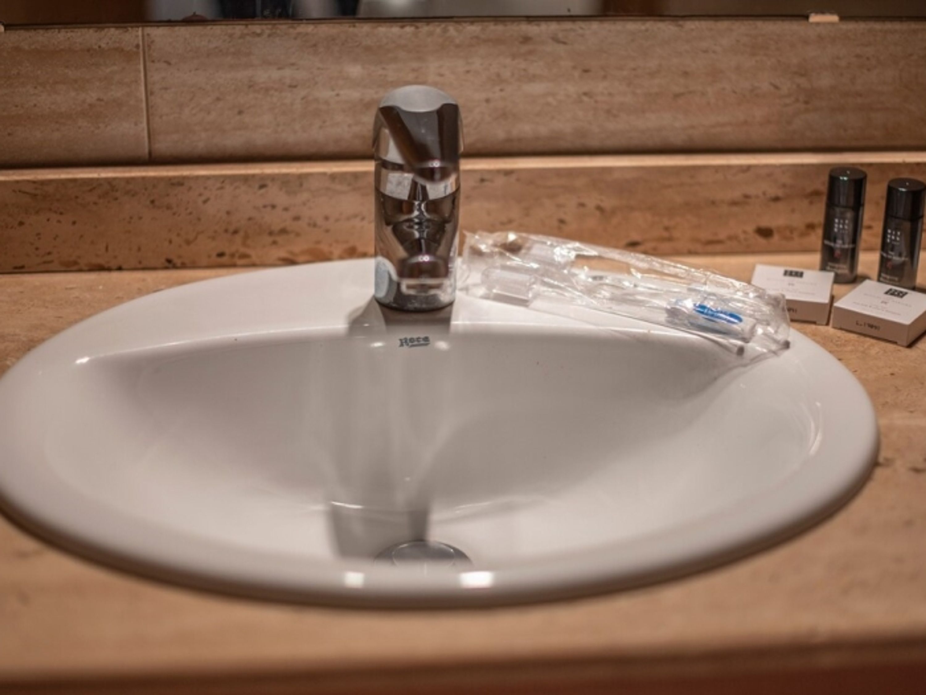 Ein weißes Waschbecken mit einem modernen Wasserhahn, eine durchsichtige Plastiktüte und verschiedene Pflegeprodukte auf der Arbeitsfläche.