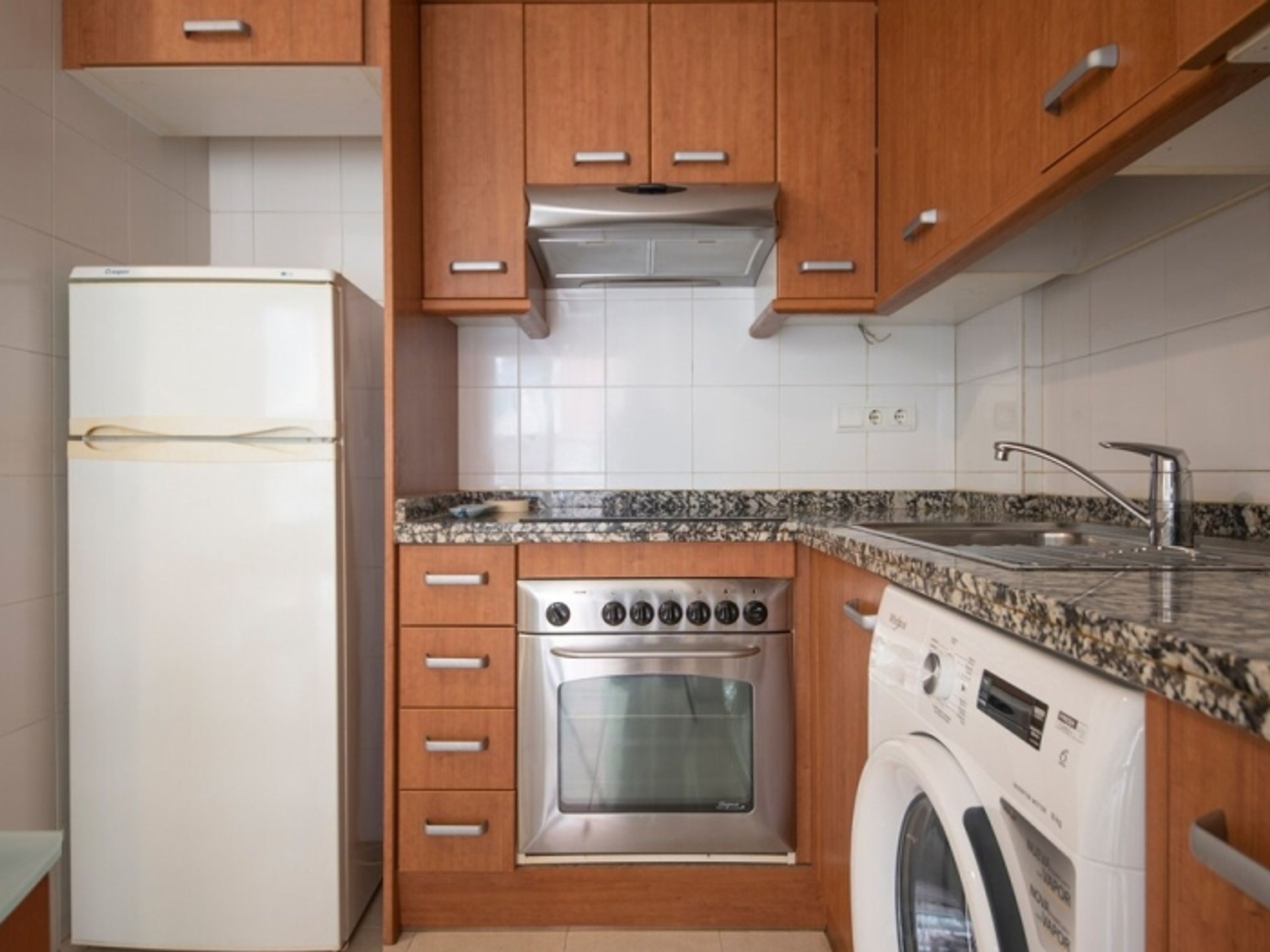 A compact kitchen with wooden cabinets, a stainless steel oven, a built-in washing machine, and a granite countertop.