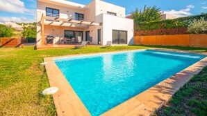 Ein modernes, zweistöckiges Haus mit Swimmingpool, Terrasse und Gartenmöbeln sowie einem gepflegten Rasen.