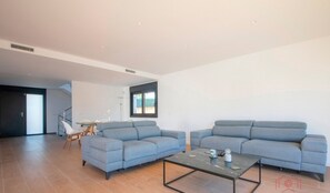 A modern living room with two grey sofas, a glass coffee table, and a wooden floor.