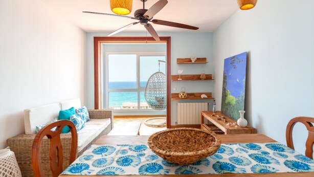A room with a view of the sea, a ceiling fan, wicker furniture, and a dining table with a patterned tablecloth. - Th163 Apartamento Via Augusta con Vistas al mar (Tarragona)