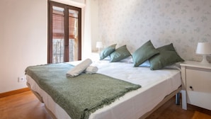 A bedroom with a large bed, a bedside table with a lamp, a window with blinds, and a patterned wall. - Th125 Atico con Vistas en Tarrgona (Tarragona)
