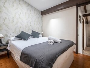 A neatly made bed with pillows, a rolled towel, and a nightstand with a lamp.