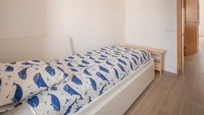 Habitación individual con una cama de una sola plaza, cabecera blanca, mesita de noche de madera y colcha estampada.
