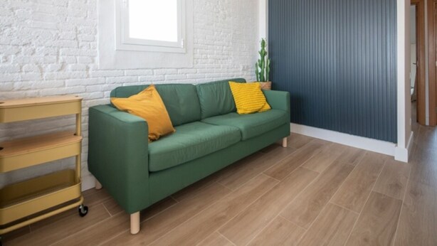 Un sofá verde con cojines amarillos, una mesita de madera y una planta en una esquina.