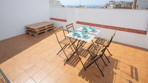 Una terraza en la azotea con una mesa para cuatro, sillas alrededor y un palé de madera apoyado en la pared.
