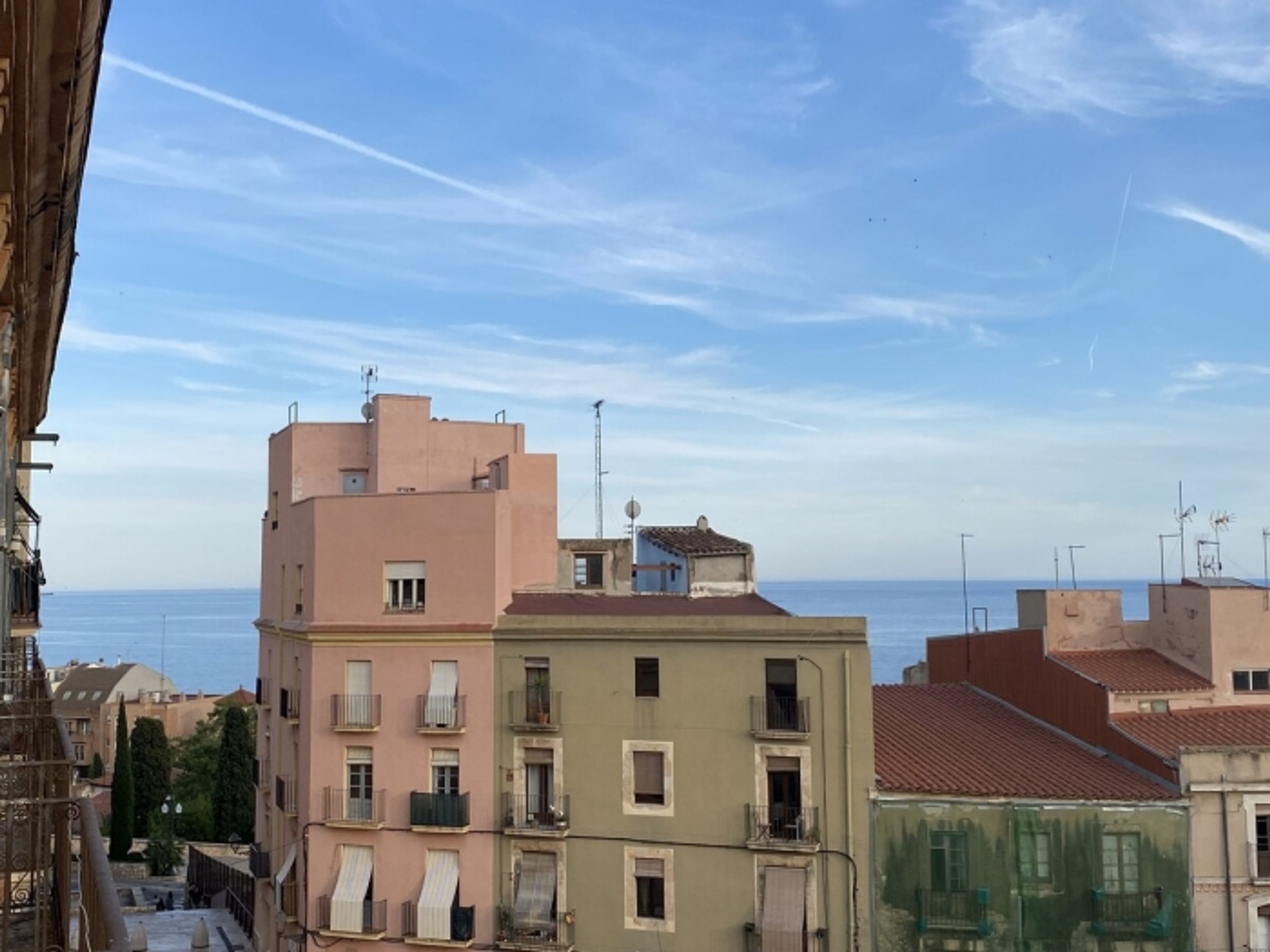 A coastal cityscape with multi-story buildings, some with balconies, under a clear sky.