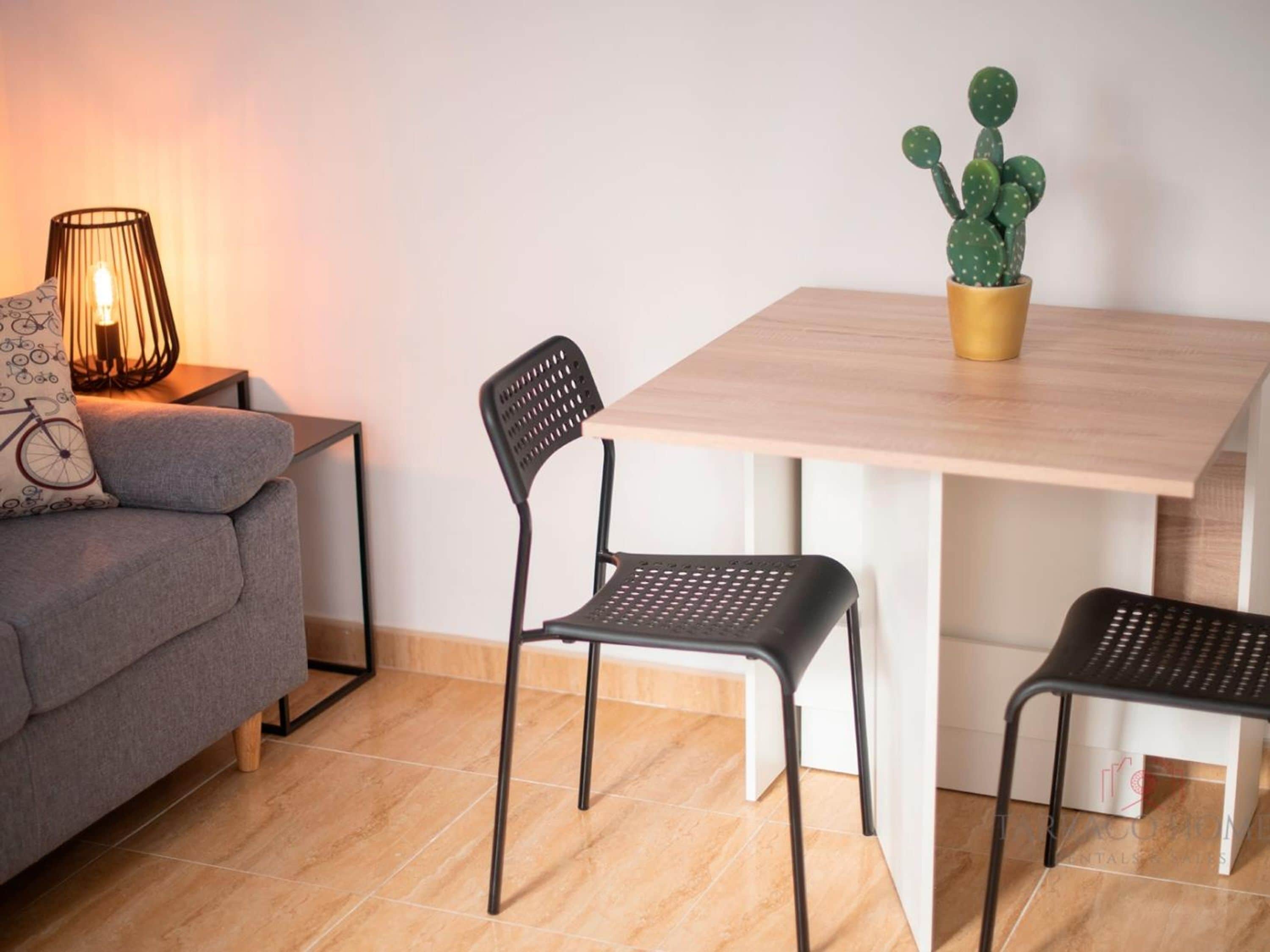 A modern living room with a sofa, two chairs, a table, a lamp, and a cactus plant.