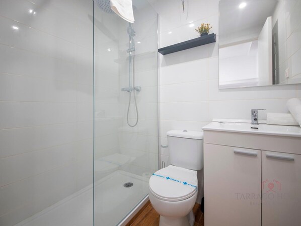 A modern bathroom with a glass shower enclosure, a white toilet, and a sink with a mirror above it. - Th08 Apartamento Moderno con Patio Privado (Tarragona)
