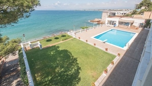 Una piscina en la azotea con vistas al mar, rodeada por un césped cuidado y una valla blanca.