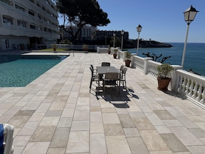 A poolside area with a table and chairs, a pool, and a view of the sea. - Th92 Apartamento en la Primera Linea en Salou (Salou)
