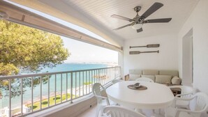 Un balcón con una mesa y sillas blancas, un ventilador de techo y vista al mar.