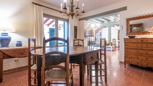 Un comedor con una mesa redonda, sillas y una araña. Se observa un aparador de madera con cajones y un espejo.