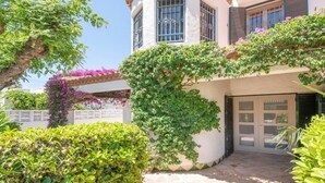 Una casa de dos pisos con fachada blanca, techo de tejas y un balcón pequeño con flores moradas.