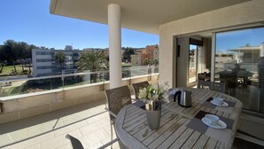 A round wooden table with two chairs, a vase with white flowers, a cup, and a thermos on a balcony with a glass railing. - Th26 Atico en Salou con Vistas y Piscina (Salou)