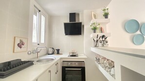 A compact kitchen with a sink, stove, and oven, a window, and a wall-mounted TV. - Th10 Apartamento Destral en el Centro de Tarragona (Tarragona)