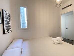 A bedroom with a bed, a window, a door, and a wall-mounted artwork.