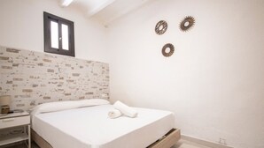 A bedroom with a wooden bed frame, white bedding, a nightstand with a lamp, and a brick-patterned wall. - Th158 Aprtamento Sedassos (Tarragona)