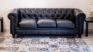 A black leather sofa with a tufted backrest and three cushions, placed on a patterned tile floor. - Th158 Aprtamento Sedassos (Tarragona)
