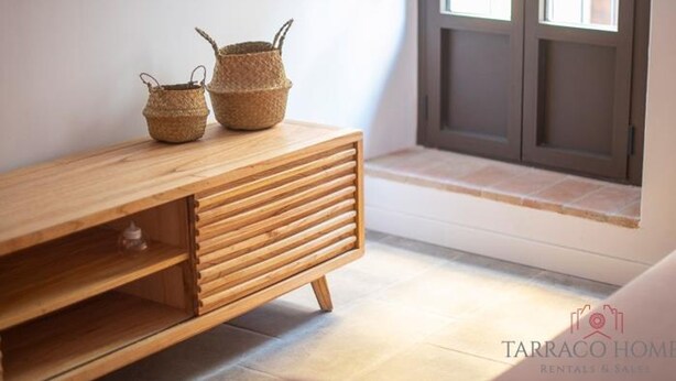 A wooden console table with woven baskets, a flat-screen TV mounted above, and a window with a view of the outside. - Th56a Apartamentos Murmur la Font (Tarragona)