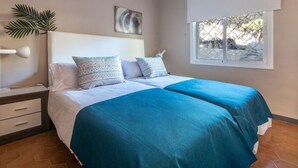 A bedroom with two beds, a nightstand, a lamp, a window with a view, and a plant. - Th123 Apartamento con Vistas al mar Cala Romana (Tarragona)