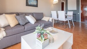 A modern living room with a grey sofa, white chairs, a white coffee table with a plant, and a painting on the wall. - Th123 Apartamento con Vistas al mar Cala Romana (Tarragona)