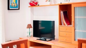A room with a wooden desk, a television, a bookshelf, and a small table.