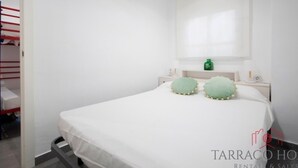 A neatly arranged bedroom with a bed, a nightstand, a green bottle, and a mirror on the wall.