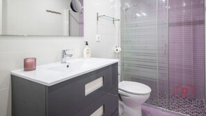 A modern bathroom with a white sink, dark cabinet, and a glass shower enclosure.