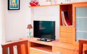 A room with a wooden desk, a television, a bookshelf, and a small table. - Th03 Apartamento Cerca de la Playa en la Pineda (Salou)