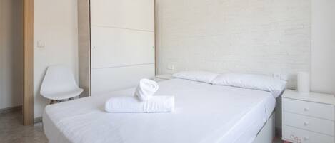 A hotel room with a large bed, a nightstand, a chair, and a wardrobe.