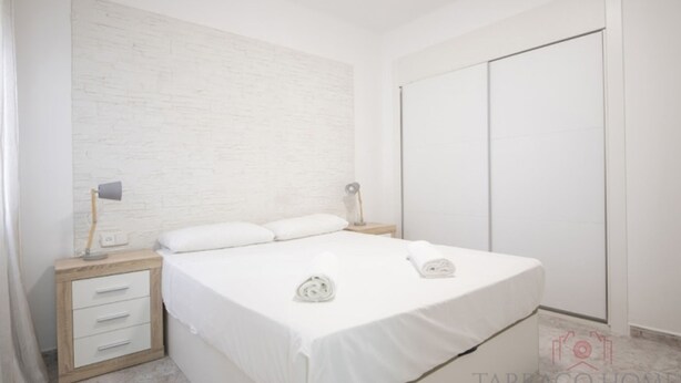 A bedroom with a bed, two bedside tables, a nightstand, a wardrobe, and a wall with a textured pattern. - Th134 Apartamento Moderno Centro de Tarragona (Tarragona)