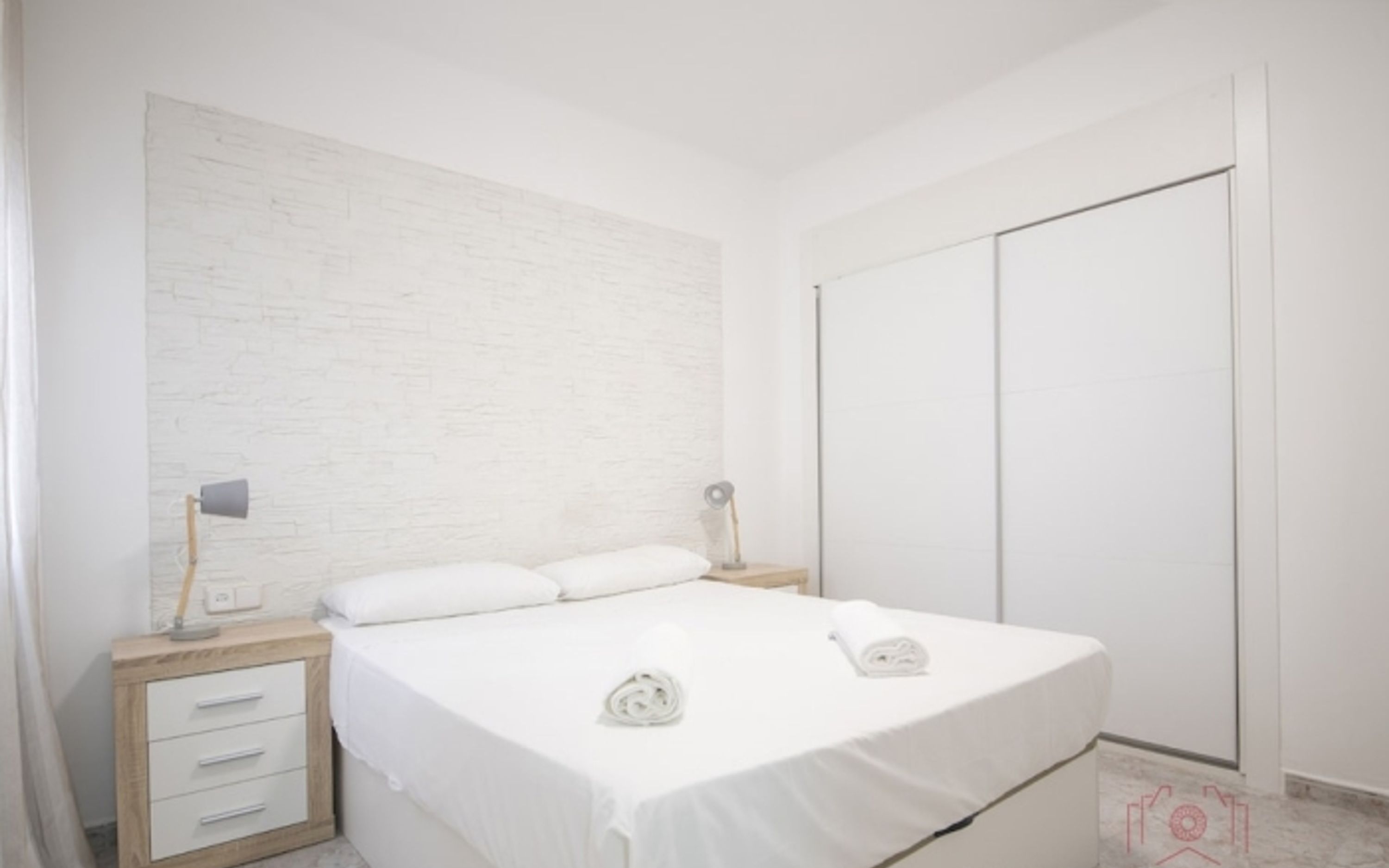 Une chambre à coucher comprenant un lit, deux tables de chevet, une commode, une armoire et un mur orné d’un motif texturé.