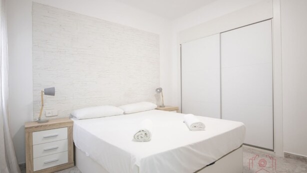 Ein Schlafzimmer mit einem Bett, zwei Nachttischen, einem Kleiderschrank und einer Wand mit strukturierter Oberfläche.