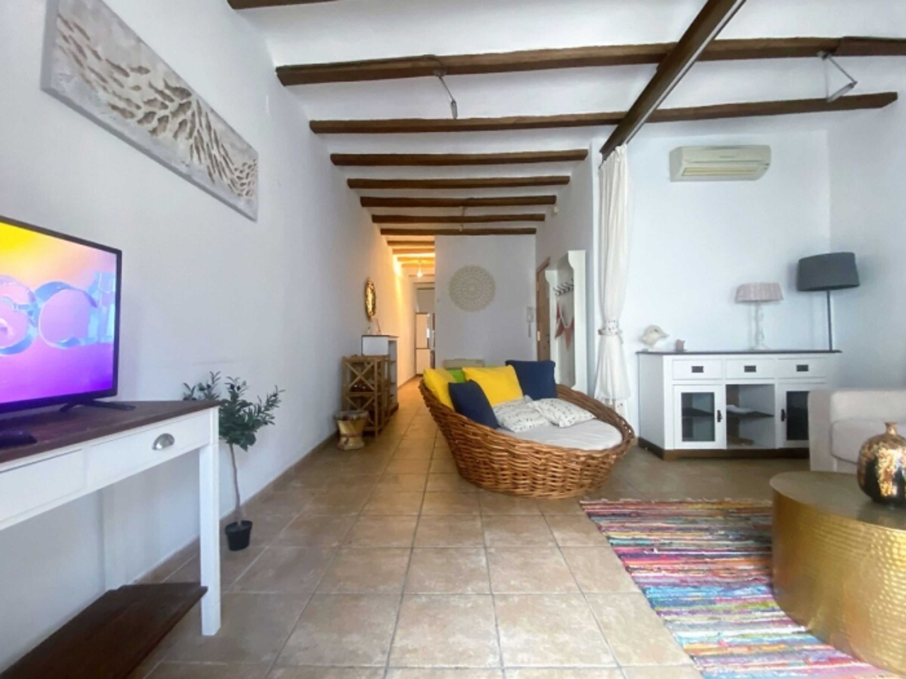 A living room with a TV, a wicker sofa, a white cabinet, and a colorful rug.
