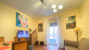 Una sala de estar con televisor, una mesa de comedor y sillas. Hay un sofá y una lámpara.