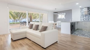 A modern living room with a white sectional sofa, a dining area, and a kitchen with a washing machine. - Th88 Apartamento en Miami Playa (Mont-roig del Camp)